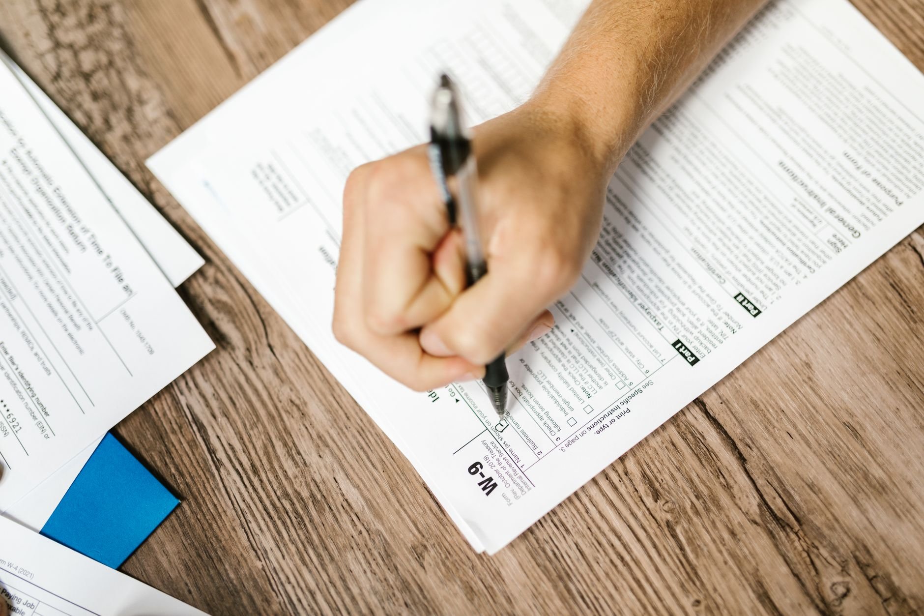 Hand writing on an invoice form at a wooden desk with a pen.